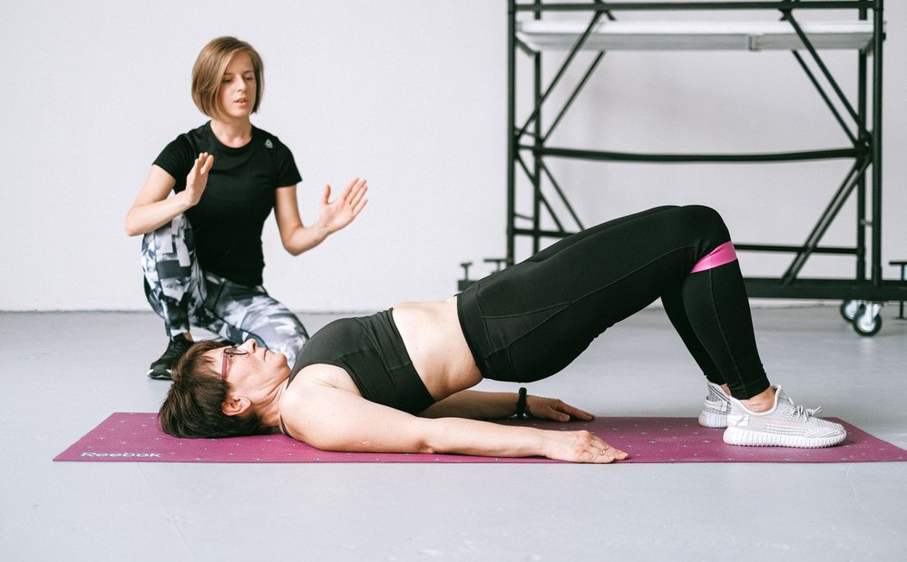 Physiotherapist guiding a patient through a bridge exercise on a floor mat